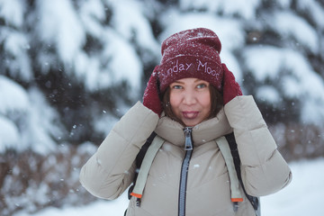 Fototapeta na wymiar People, season and holidays concept - portrait of happy smiling young woman outdoors in winter park. She clothed in red winter hat and red mittens. Snowy weather.