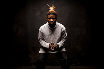 Black man with blonde dreadlocks posing holding fingers together on the bending knees