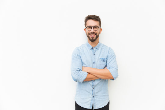 Joyful positive guy posing with arms folded. Handsome young man in casual shirt and glasses standing isolated over white background. Happy man portrait concept