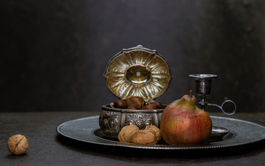 Obraz na płótnie Canvas Pear, chestnuts and walnuts on a background of silver vintage accessories
