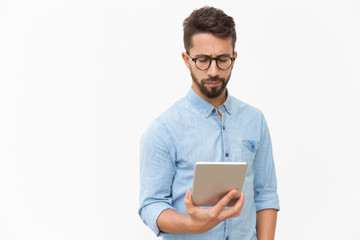 Serious entrepreneur checking email on tablet. Handsome young man in casual shirt and glasses standing isolated over white background. Wireless internet technology concept