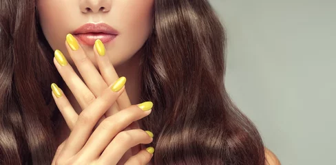 Foto auf Acrylglas Schönes Mädchen langes, lockiges Haar. Vorbildliche Frau, die eine gelbe Maniküre auf den Nägeln zeigt. Kosmetik und Make-up © Sofia Zhuravetc