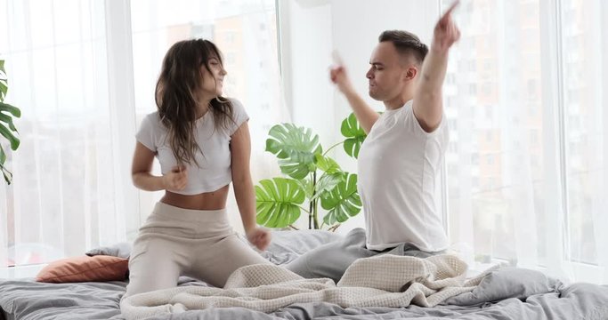 Young couple having fun dancing on bed at home