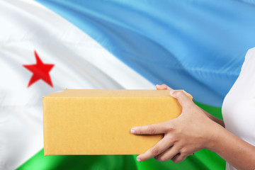 Djibouti delivery service. International shipment theme. Woman courier hand holding brown box isolated on national flag background.