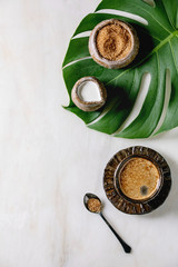 Ceramic cup of espresso coffee serving with cane sugar, jug of cream standing on monstera leaf over...