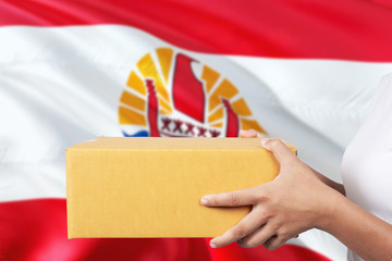 Fototapeta premium French Polynesia delivery service. International shipment theme. Woman courier hand holding brown box isolated on national flag background.