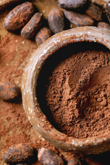 Cocoa powder in ceramic bowl with cocoa beans over brown texture background. Flat lay, close up