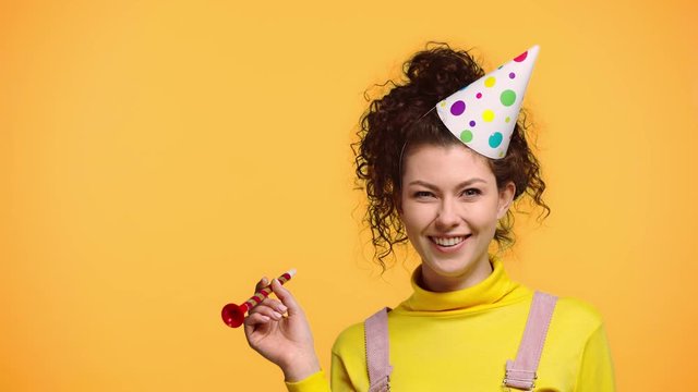 happy woman blowing in party blower isolated on orange