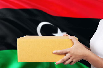 Libya delivery service. International shipment theme. Woman courier hand holding brown box isolated on national flag background.