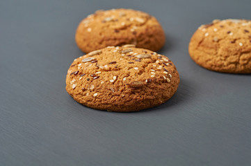 Three fresh homemade cookies with seeds of sunflower and sesame in form of triangle lies on dark scratched concrete table on kitchen. Close-up