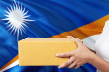 Marshall Islands delivery service. International shipment theme. Woman courier hand holding brown box isolated on national flag background.
