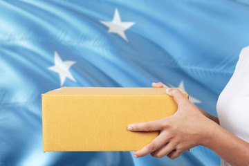 Obraz premium Micronesia delivery service. International shipment theme. Woman courier hand holding brown box isolated on national flag background.