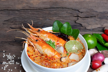 Tom Yum Goong or Shrimp soup spicy sour Soup Traditional food in Thailand contains chili, lime,lemongrass, lime leaf, along with cooked rice in a white dish on the old wood background.