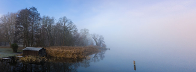 Panorama von Bootshaus mit Schilf und Nebel am Ruppiner See im Winter