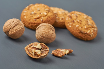 Walnuts beside homemade cookies with seeds of sunflower and sesame lies on dark scratched concrete table on kitchen. Close-up