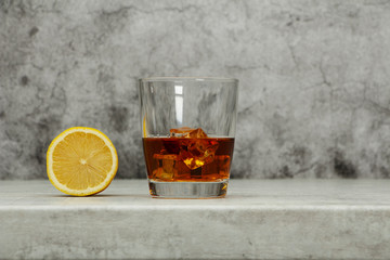 Whiskey with ice or brandy in a glass with lemon on a background of gray concrete on an old wooden table. Whiskey with ice in a glass. Whiskey or brandy. Selective focus.