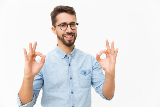 Happy joyful guy showing OK gesture with both hands. Handsome young man in casual shirt and glasses standing isolated over white background. Customer satisfaction concept