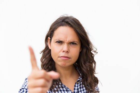Strict frowning Latin woman shaking finger at camera. Young woman in casual checked shirt standing isolated over white background. Threaten gesture concept