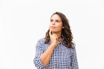 Pensive student girl touching chin and looking away at copy space. Young woman in casual checked shirt standing isolated over white background. Decision making concept