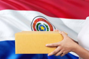 Paraguay delivery service. International shipment theme. Woman courier hand holding brown box isolated on national flag background.