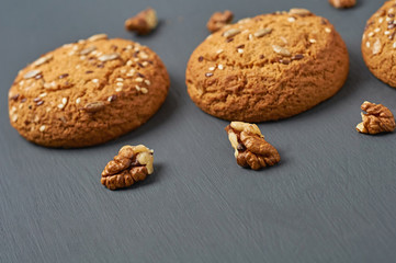 Walnuts beside homemade cookies with seeds of sunflower and sesame lies on dark scratched concrete table on kitchen. Space for text