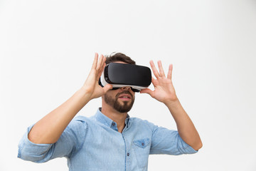 Bearded male user in VR glasses enjoying experience. Young man in virtual reality headset standing isolated over white background. VR game test concept