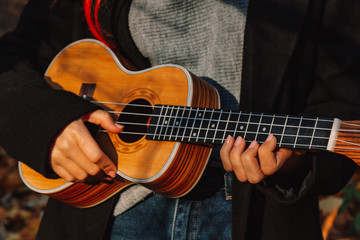 Fototapeta na wymiar Red-haired girl with long hair plays on the ukulele in the park. School, music education concept, student learns to play the string instrument. Hands of a musician, classical, melody, creativity.
