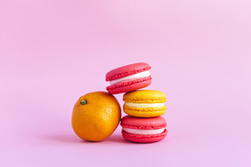 Three tasty french macarons and tangerine on pink background.  Close-up.