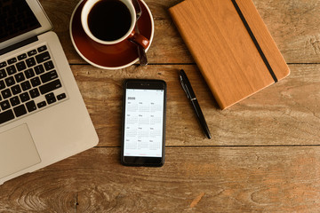 Screen of smartphone with calendar of year 2020 with laptop, pen and note book on coffee table