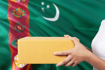Turkmenistan delivery service. International shipment theme. Woman courier hand holding brown box...