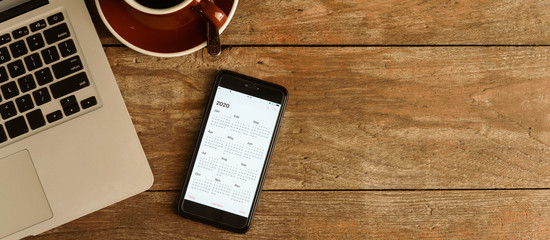 Screen of smartphone with calendar of year 2020 with laptop, pen and organizer on coffee table - Powered by Adobe