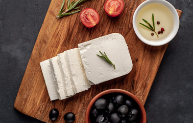 feta cheese, with rosemary, tomatoes, olives on a stone background