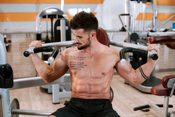 Muscular athletic young man bodybuilder fitness model focusing on exercise with in the gym