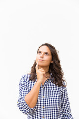 Fototapeta premium Thoughtful student girl touching chin and looking up at copy space. Young woman in casual checked shirt standing isolated over white background. Advertising concept