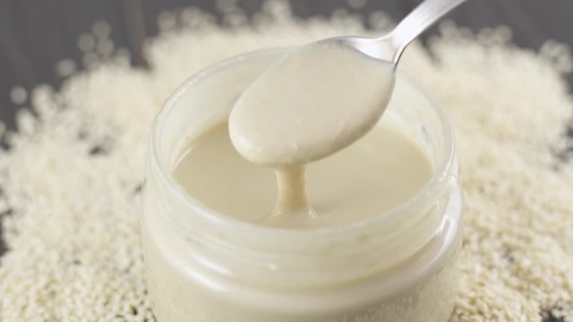 Sesame butter, tahini. Creamy paste from white sesame in jar on a table. Spoon on Natural nutrition and organic food.