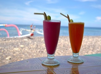Organic fruit cocktail on sandy beach with sea on background.