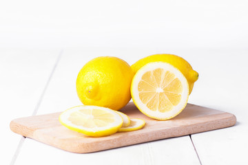 Ripe full yellow lemon citrus fruit with lemon half and lemon's slicees on white wooden background. Full depth of field. Copy space