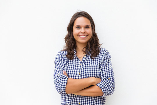 Happy joyful student girl with arms folded looking at camera and smiling. Young woman in casual checked shirt standing isolated over white background. Female portrait concept