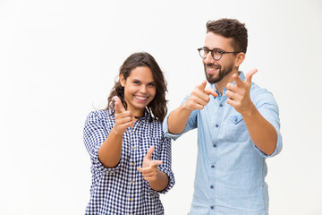 Cheerful positive couple pointing fingers at camera. Young woman in casual and man in glasses...