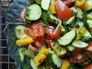 Vegetable salad of sliced yellow sweet pepper, tomatoes, dill, parsley, garlic, green onions and cucumber pieces. Seasonal food with plenty of vitamins, suitable for vegans and vegetarians.