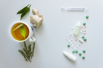 Cup of hot tea with ginger and rosemary. Pills, medicines and thermometer on a light background. Concept - prevention of colds and flu, patient care. Selective focus.