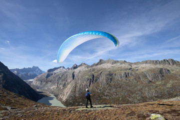 Paraglider pilot stands on a rock and balances his paraglider above his head near Lake Grimsel in...