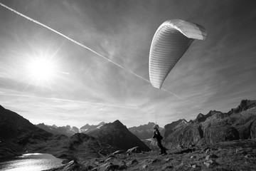 Paraglider Pilot stands on a slope and balances his paraglider above his head in the Alps of...