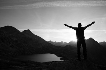 Hiker is standing on a rock with raised hands and enjoying sunrise in the Alps in Switzerland - 307913203