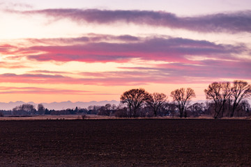 Plowed field at sunset with distant mountains and clouds