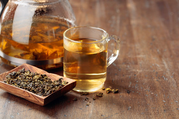 Hot green tea in glass mug. Dried tea leaves and hot drink on a wooden table.