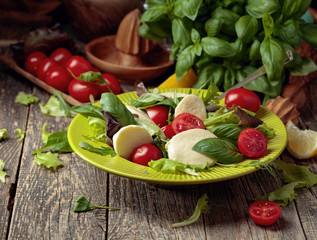 Fototapeta na wymiar Green salad with mozzarella, tomato and basil in green plate on a old wooden background.