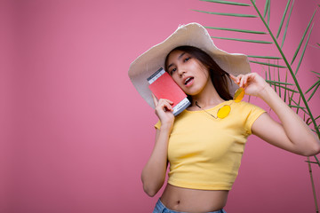 Beautiful girl in a huge white hat with a passport in her hands in glasses is going on a trip and rejoices in a yellow T-shirt and pink background