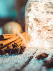 Christmas setting with bundle of cinnamon, jar with lights, anise stars and other christmas decorations on the rustic wooden background. Selective focus. Shallow depth of field.