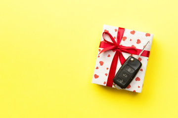 Car key on paper gift box with red ribbon bow and heart on yellow table background. Holidays present top view concept